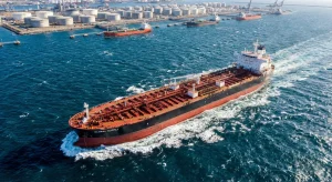 Aerial view of a massive oil tanker ship navigating the ocean towards a busy industrial port.